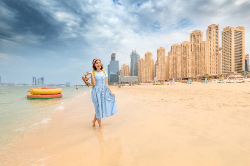 Cheerful woman takes off her sandals and walks barefoot on the water on the beach in Dubai at the Jumeirah Beach residence. The concept of travel and vacation in the UAE