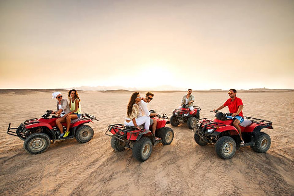 Group of young people having fun in the desert while driving on quad bikes. Copy space.